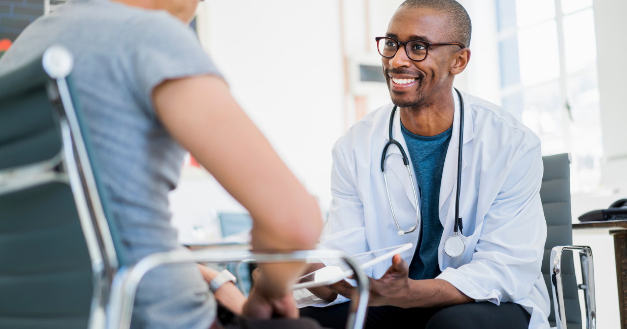 A male doctor speaks to a male patient with a smile on his face. 