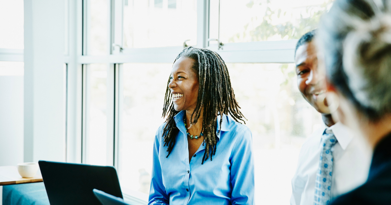 A Black woman laughs in a meeting with her laptop open in front of her. 