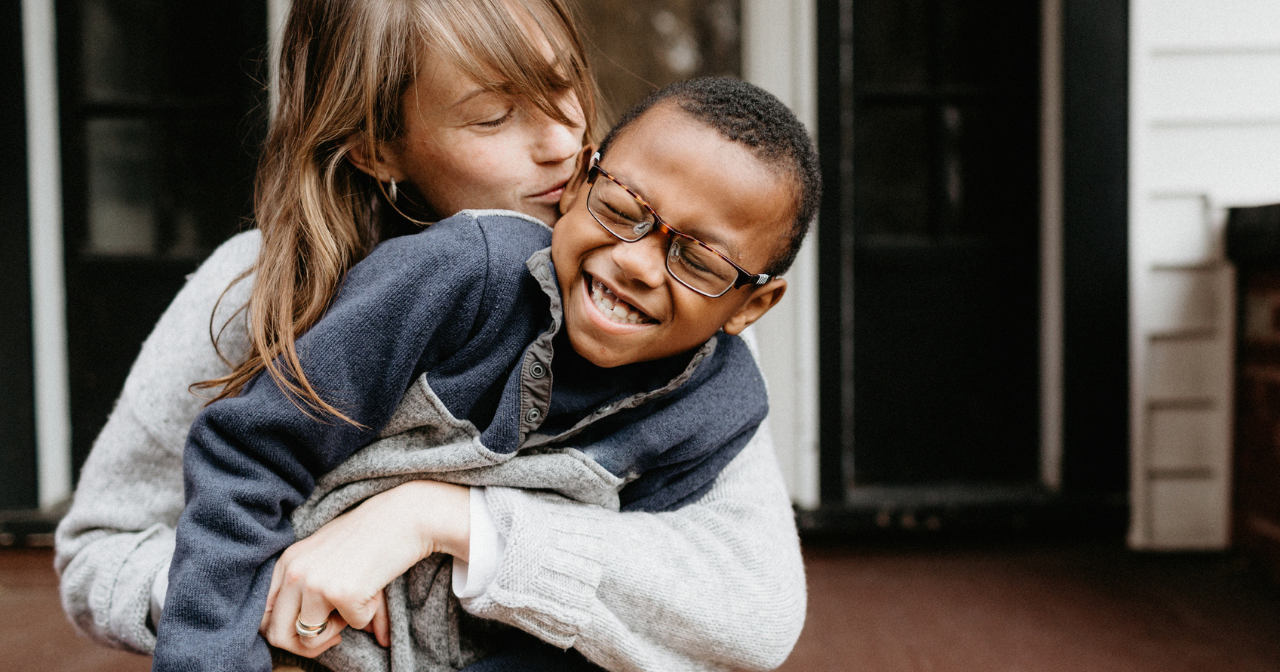 A mother and her son hug and laugh while sitting on their front step. 