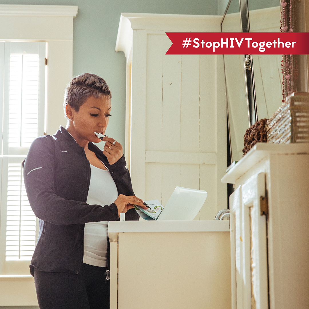 A woman stands in her bathroom and reads the instructions on an at-home HIV testing kit. 