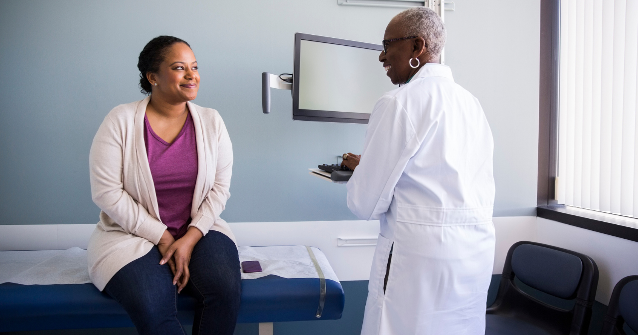 Two Black women, one a provider and one a patient, greet one another at the start of a health care visit. 