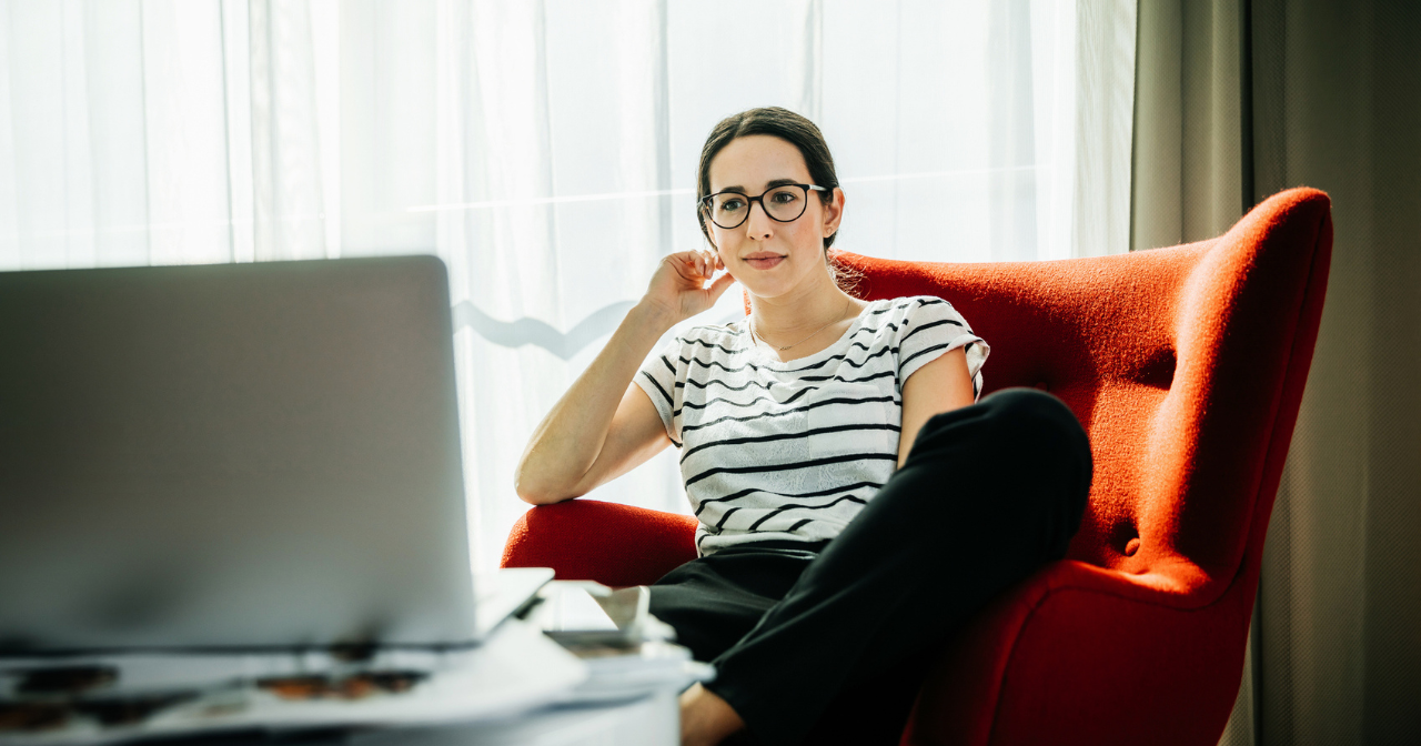 A woman sits in a chair and watches a video on her laptop. 