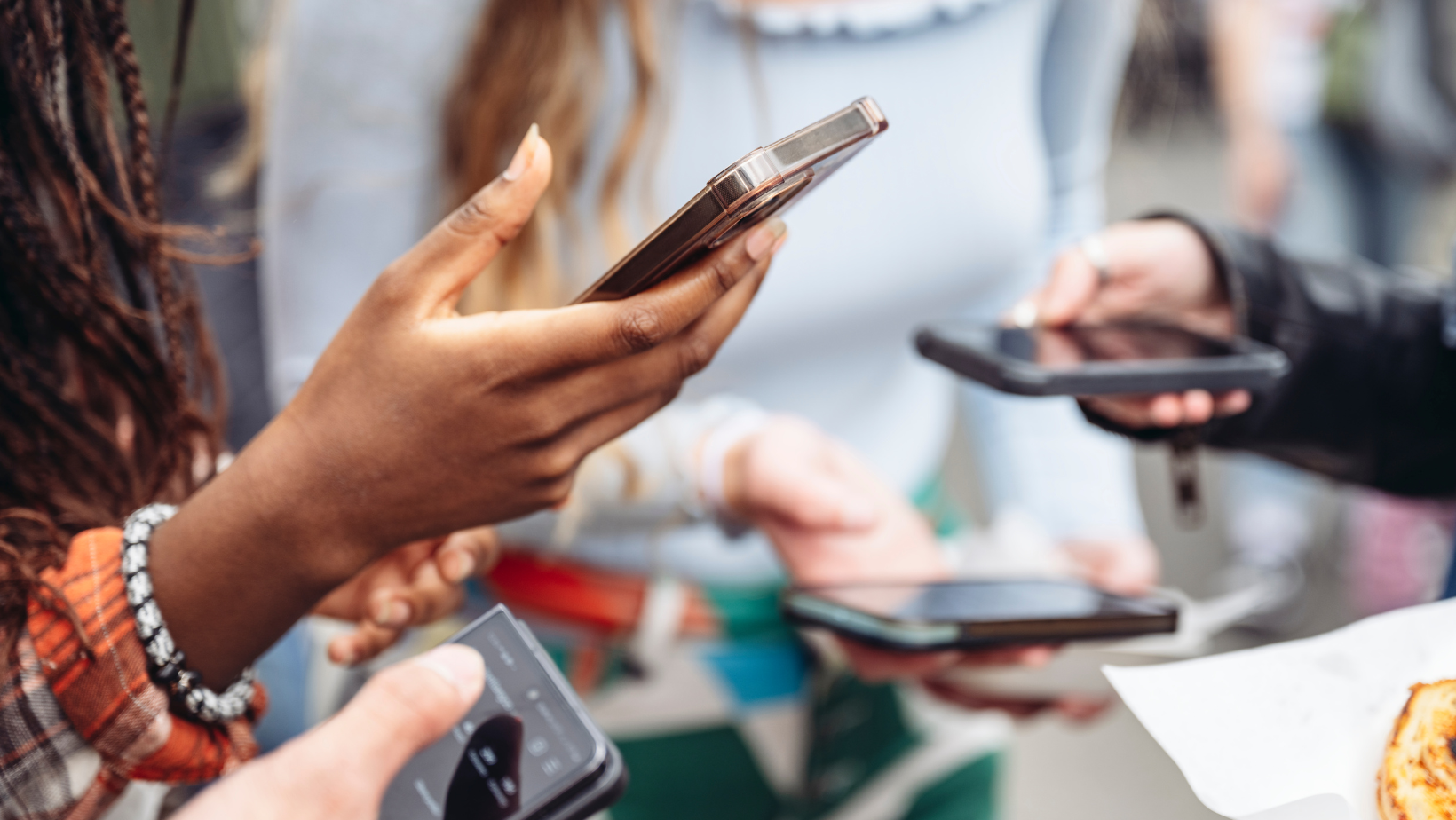 A group of friends stand in a circle all with their hands out and looking at their phones.