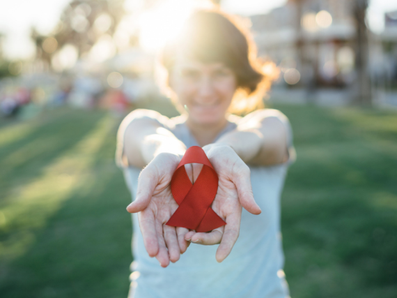 A young woman holding out an AIDS ribbon
