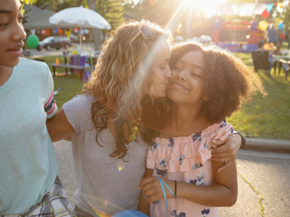 A mother kisses one daughter while hugging other daughter.