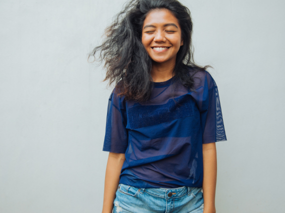 A woman smiles with her eyes closed against a blank background. 