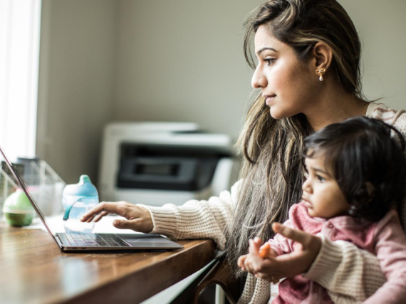 A mother holds her young child on her lap while sitting in front of a laptop. 