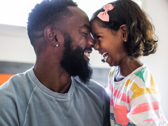 A Black father and his young daughter smile and hug. 
