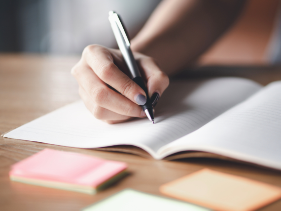 A hand holds a pen over a blank sheet of paper.