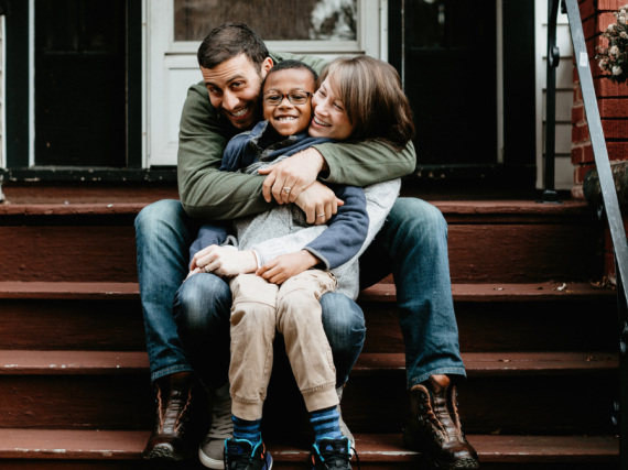 A happy family laughs and smiles sitting on the front stairs of their house.